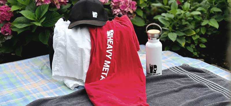Branded and United Metal Shirts, eine gebrandete Trinkflasche und eine Cap als Lifestyle-Set in einer entspannten Outdoor-Umgebung.